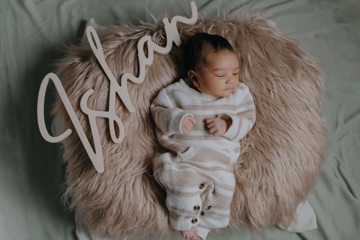 Newborn baby sleeping peacefully on fluffy beige blanket with name written above.