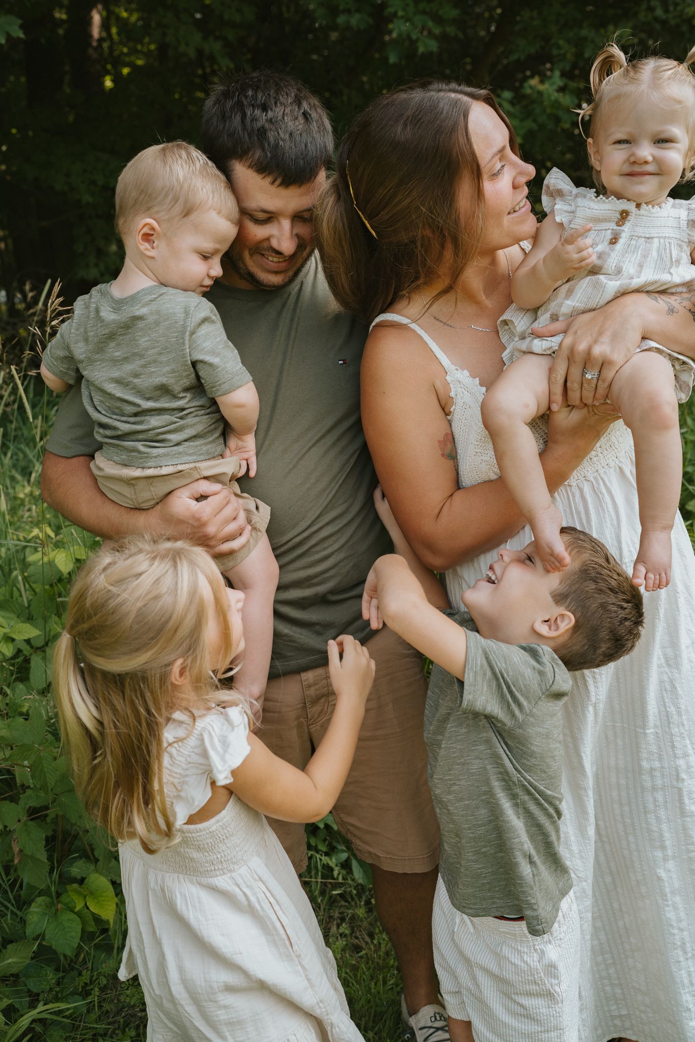 A family shares tender moments together in a series of outdoor portraits against a green backdrop.
