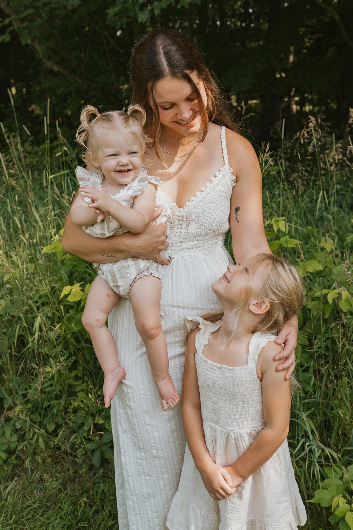 A tender moment captured outdoors showing a parent and child wearing matching white dresses against a lush green background.