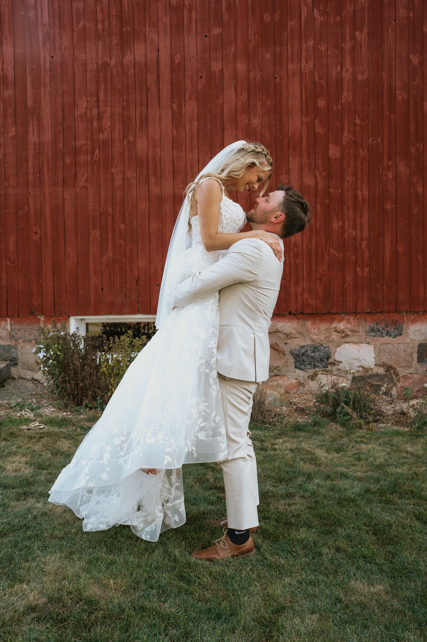 A romantic wedding couple embraces against a rustic red barn backdrop in a series of intimate poses.