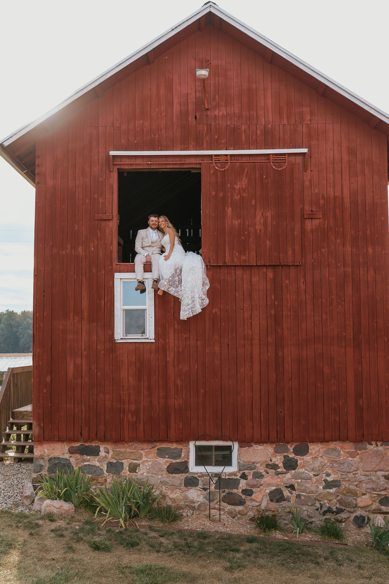 A series of four connected red barn sections with stone foundations and white trim windows against a rural landscape.