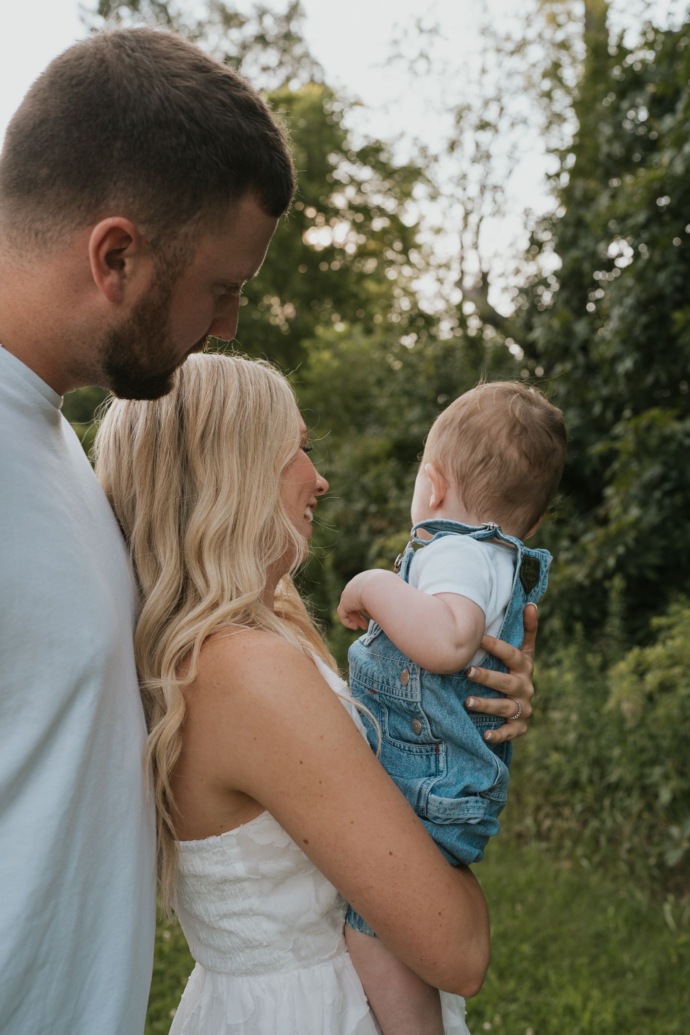 Family of three sharing tender moments together in a green summer setting in Jackson County MI