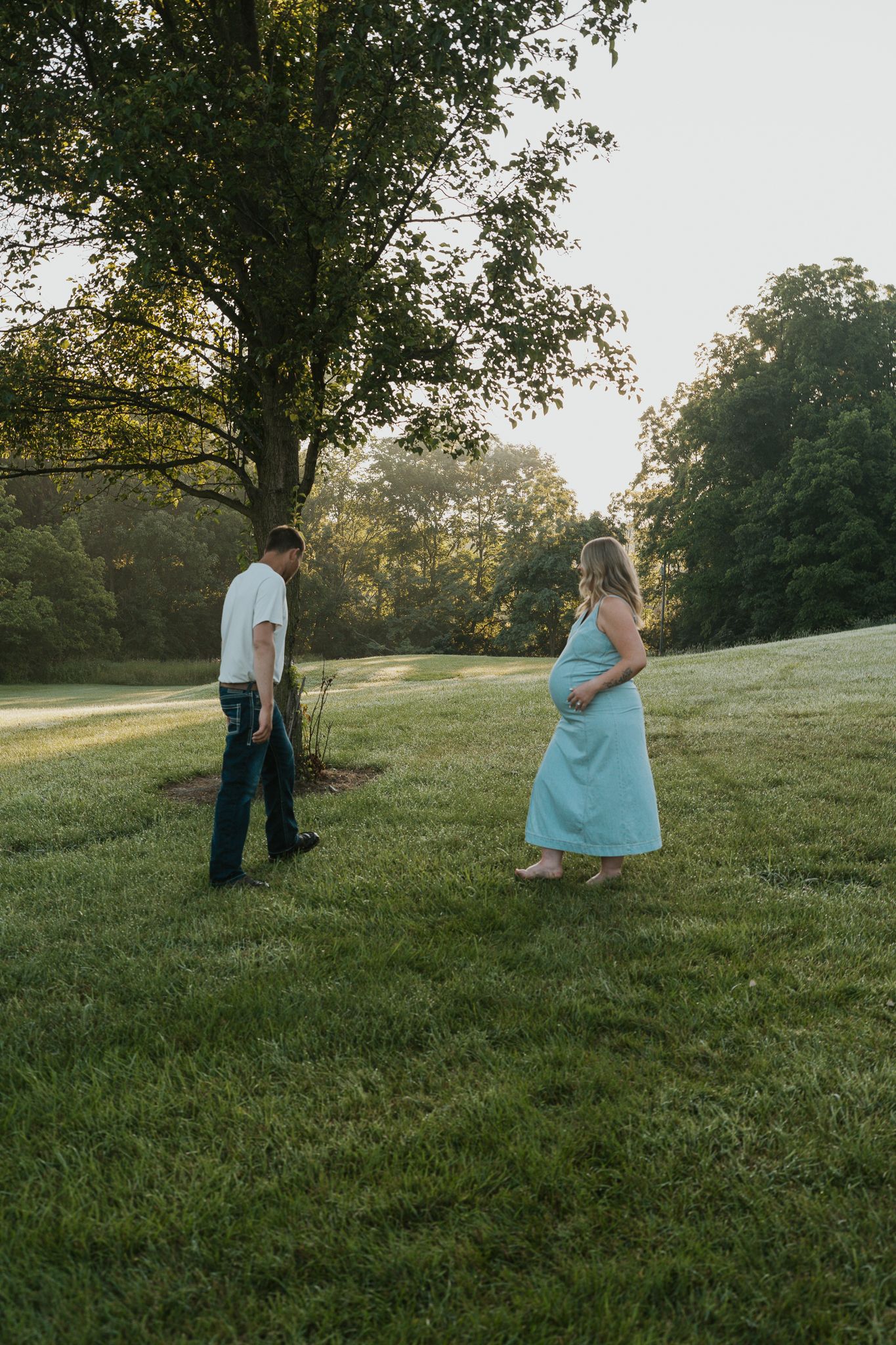 A couple stands together on a grassy hillside during golden hour in a peaceful outdoor setting.