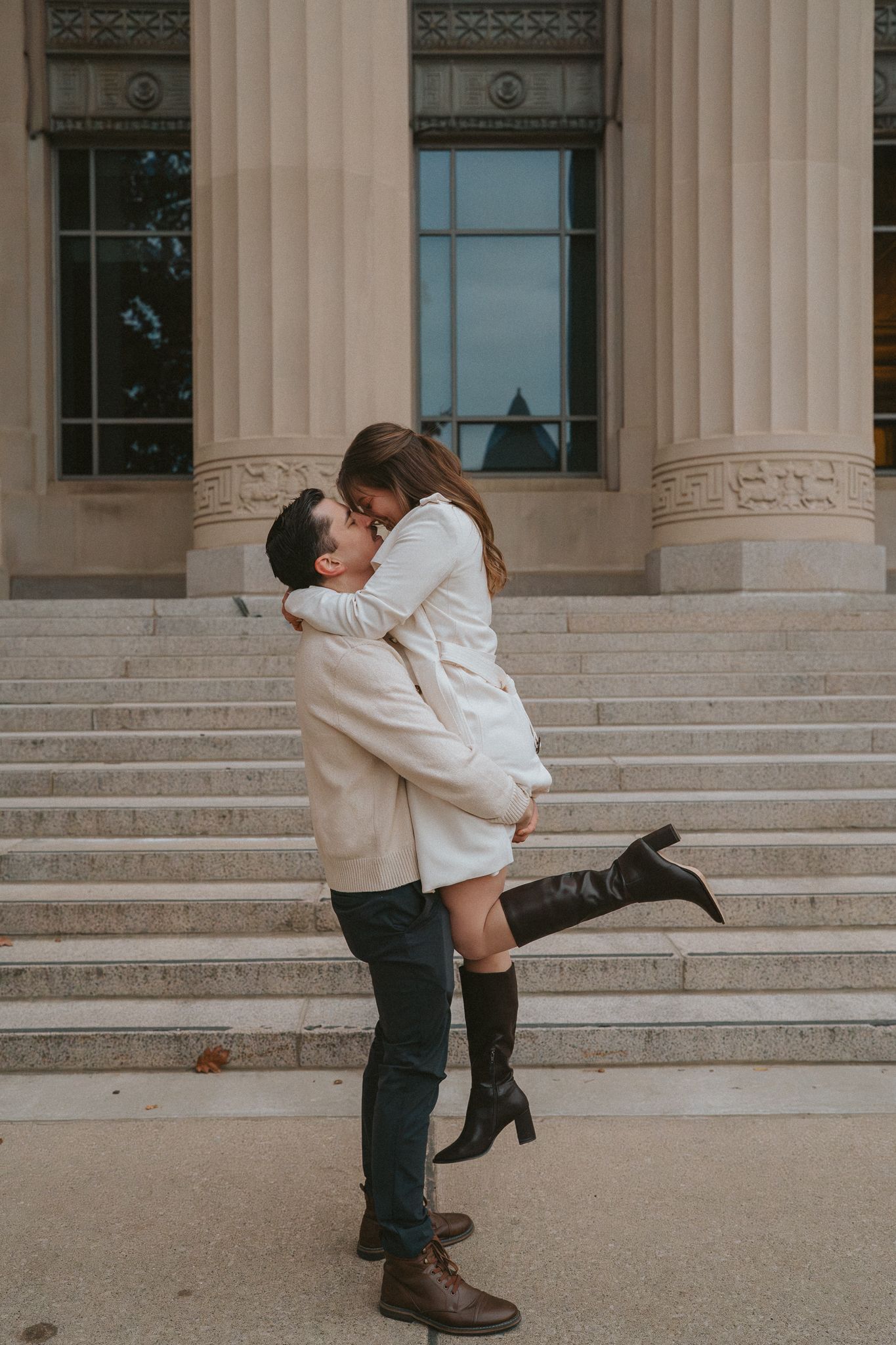 A romantic couple embraces and dips in a dance pose on stone steps in front of a neoclassical building.