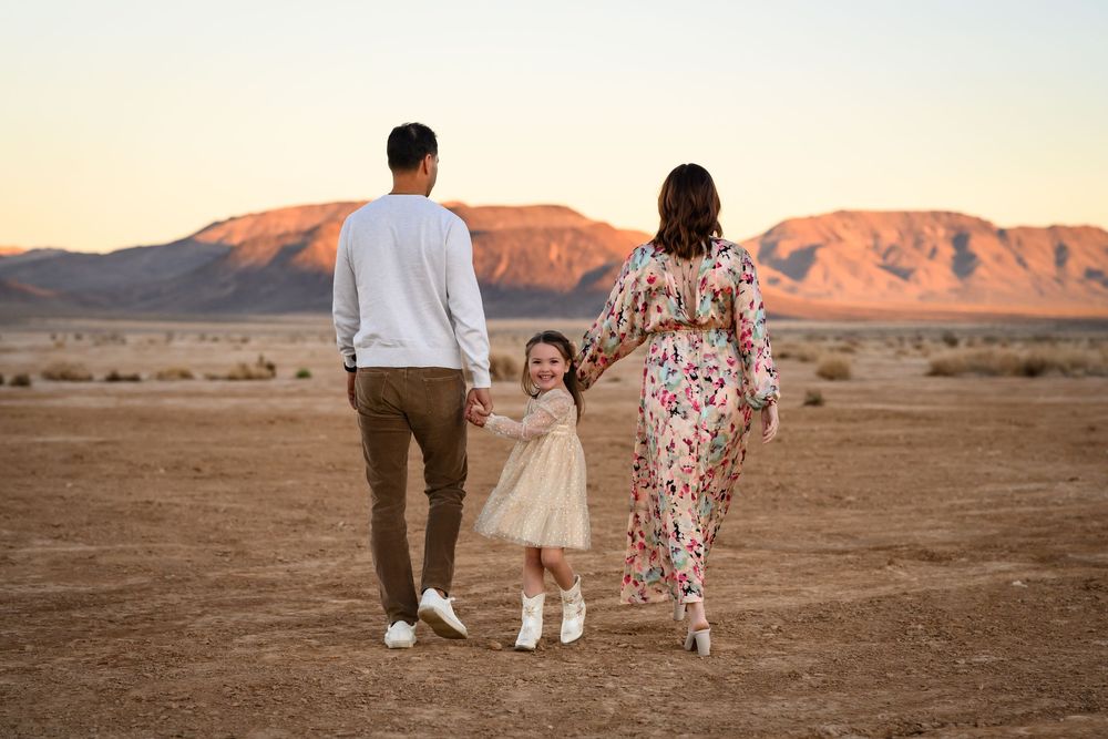 A family walks together across a desert landscape at sunset with mountains in the background. Family photographer Las Vegas