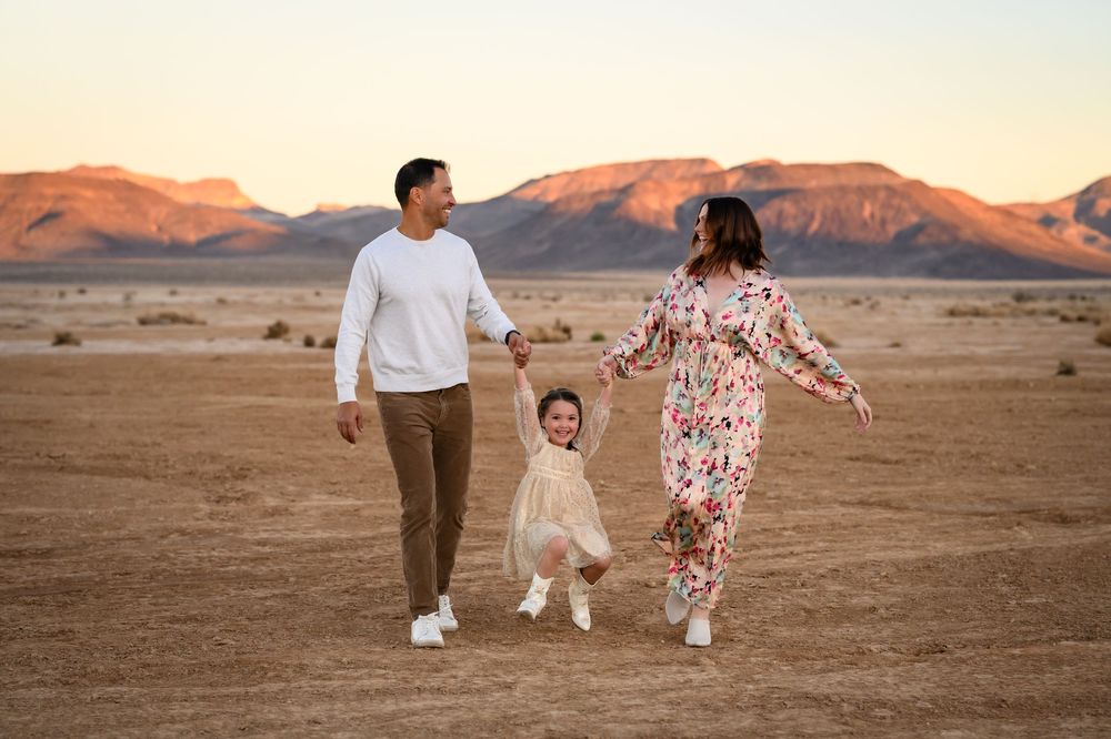 A family walks together holding hands in a desert landscape at sunset with mountains in the background. Family photography Las Vegas