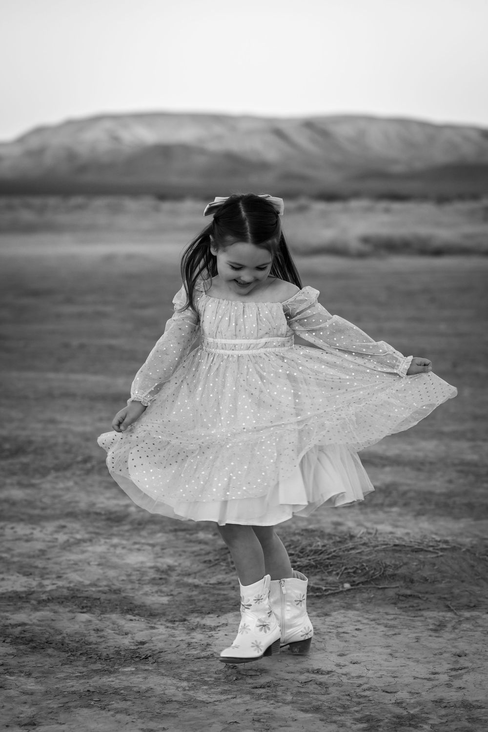 A young girl in a flowing dress twirls joyfully in front of mountain scenery in black and white photography. Family Photography Las Vegas.