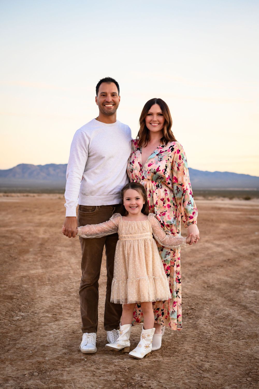 Three people in coordinated white and floral outfits pose together in a desert landscape at sunset. Family Photography Las Vegas.