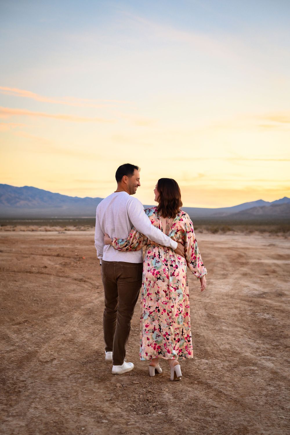 A couple walks together on a desert plain during sunset with mountains visible in the background. Family Photography Las Vegas.