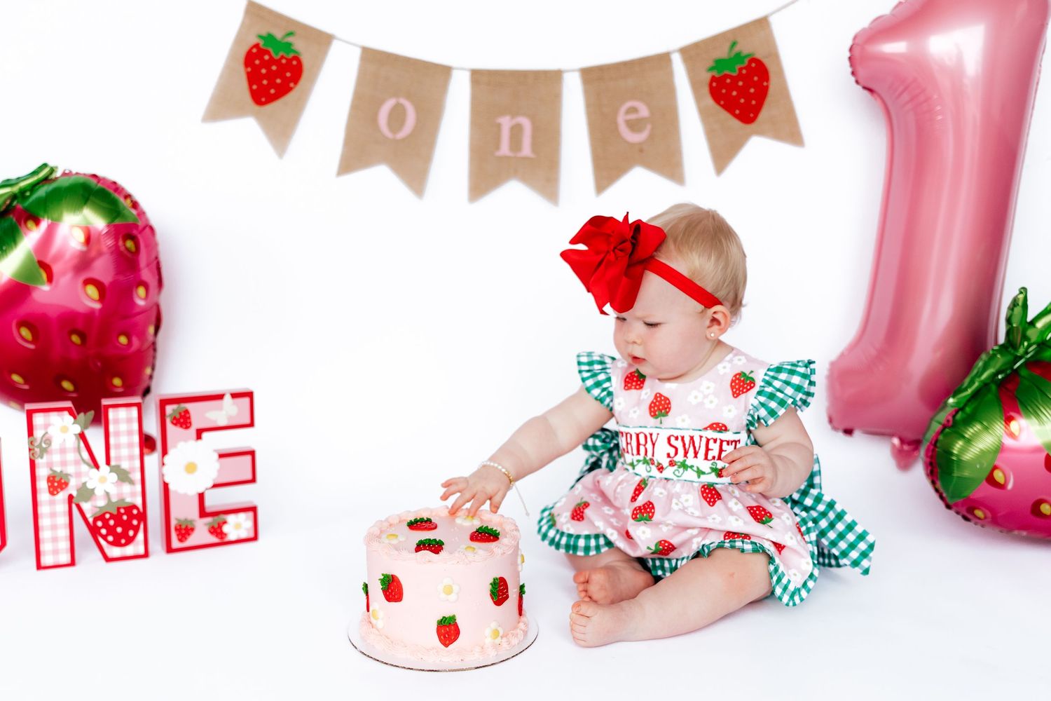 Baby in black outfit reaching for cake on yellow blanket during cake smash photo session.