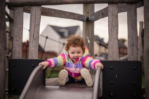 Happy smiling toddler at the top of the slide wearing brightly coloured clothes, casual and relaxed family photography