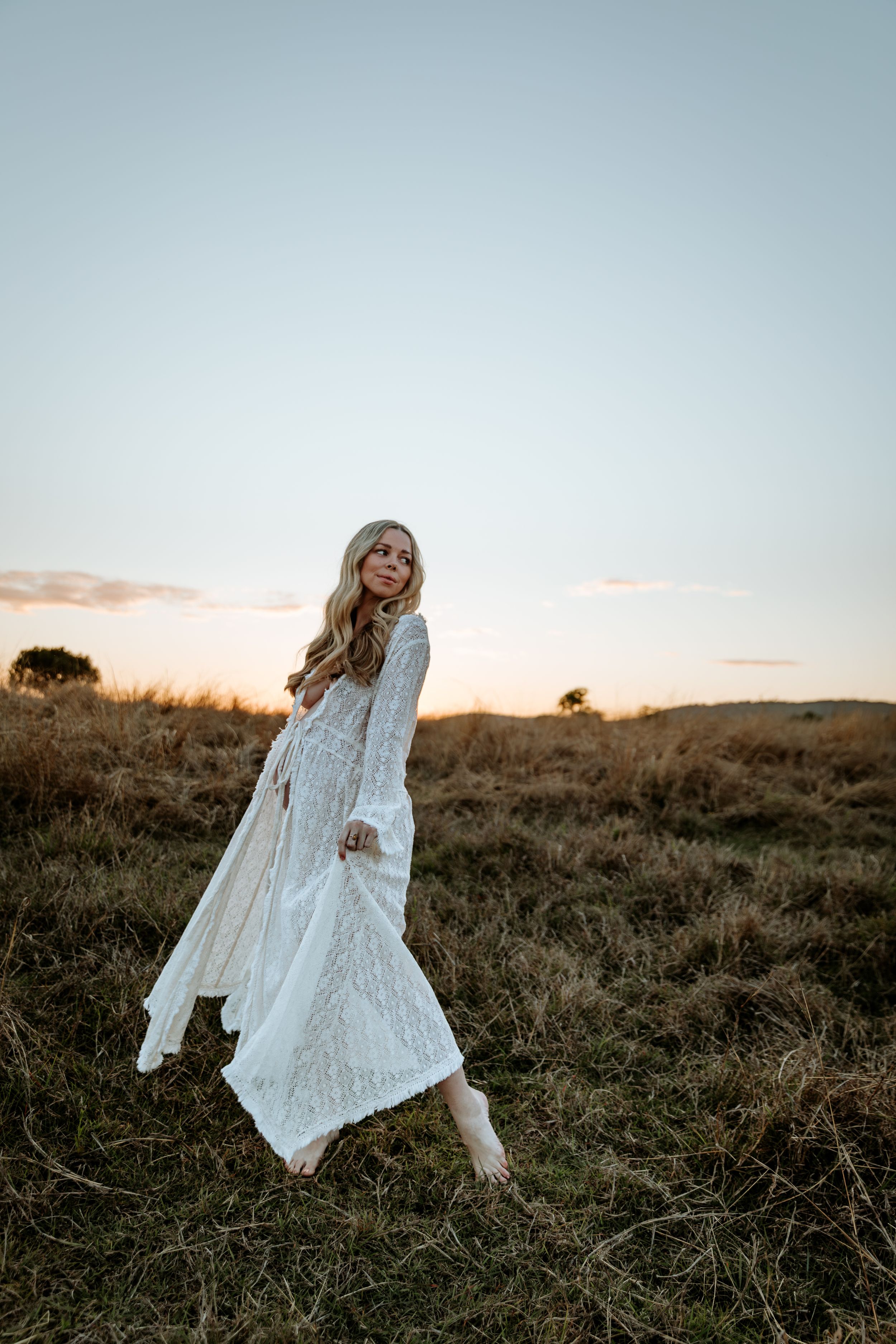 Person in flowing white dress twirls playfully in a sunset field.