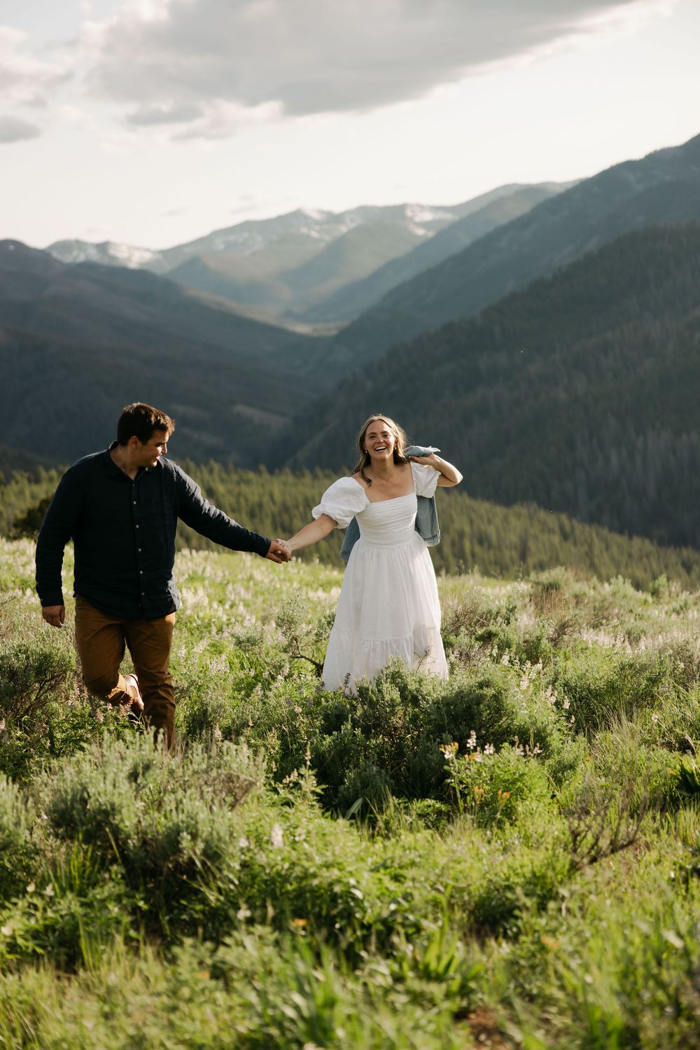 Couple walking through wildflowers on a mountainside with dramatic valley views.