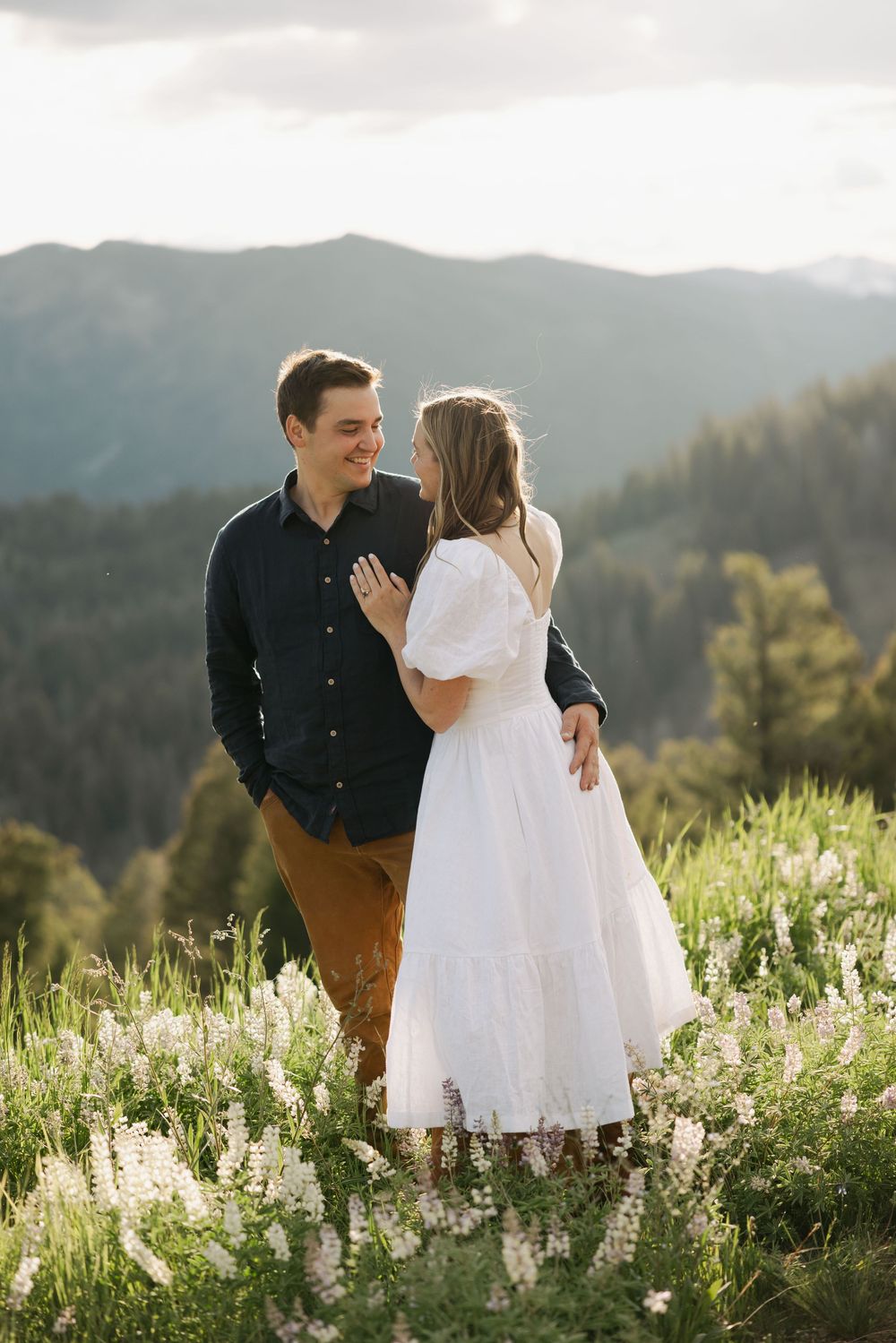 Couple standing in a mountain meadow filled with white wildflowers at sunset.