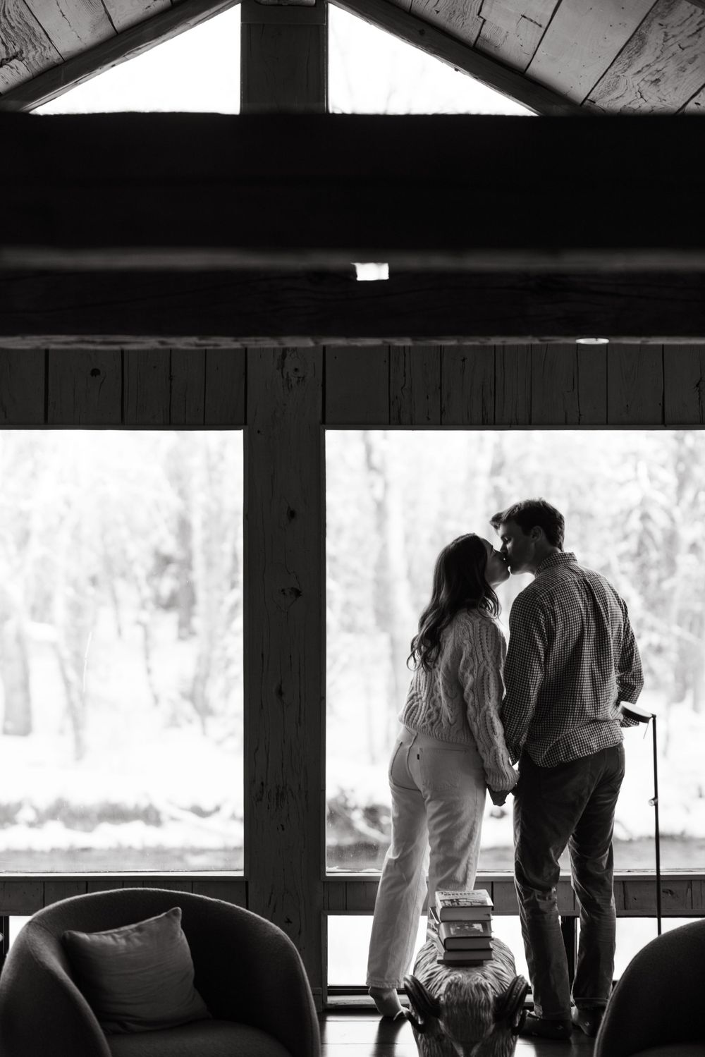 People gather by large windows overlooking a snowy landscape in a rustic wooden building.