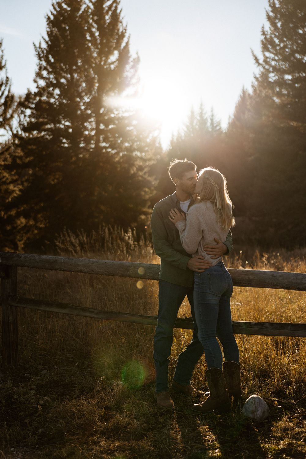 Silhouetted couple embracing at sunset with evergreen trees in the background.