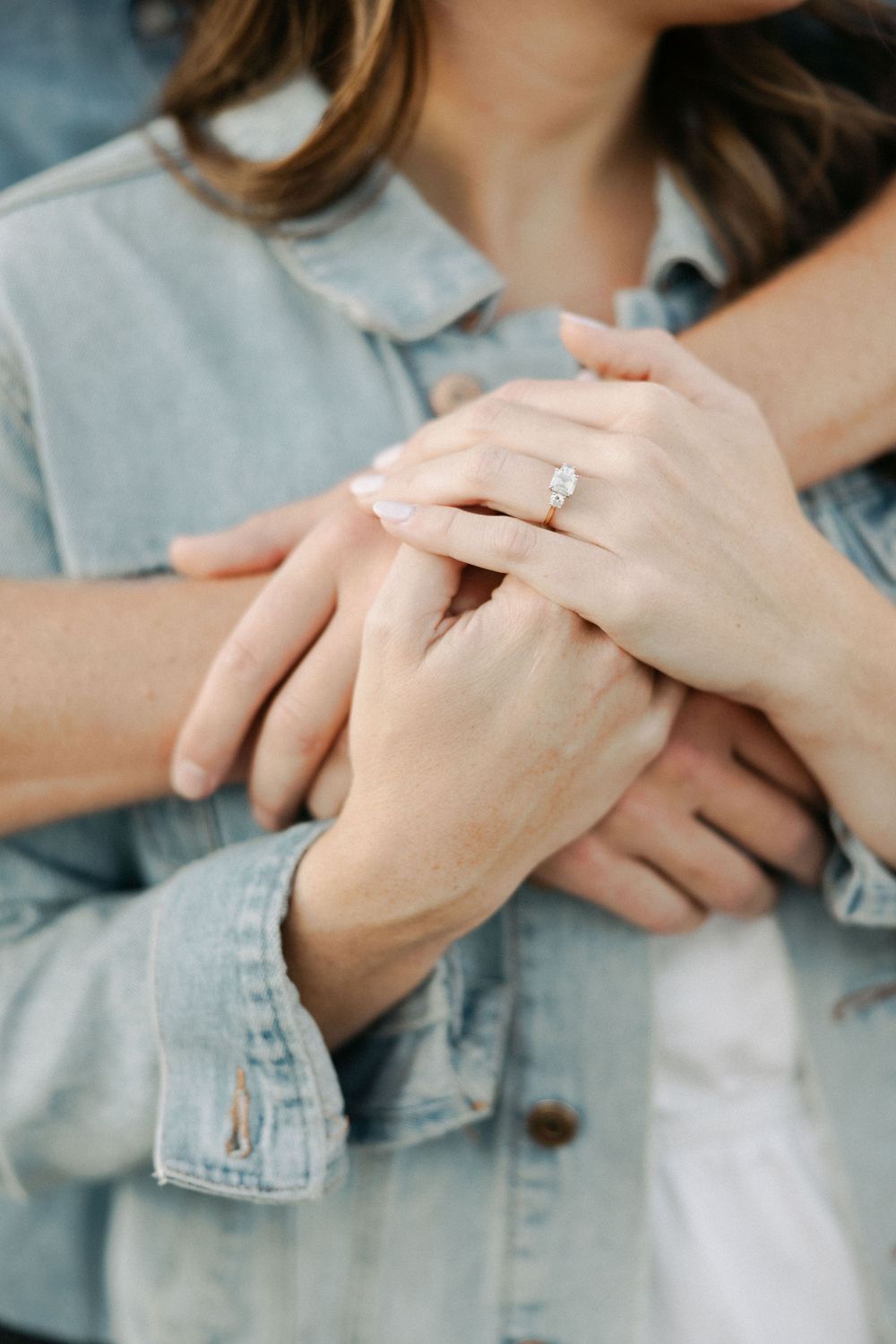 Close-up of hands showing engagement ring with denim jacket sleeve detail.