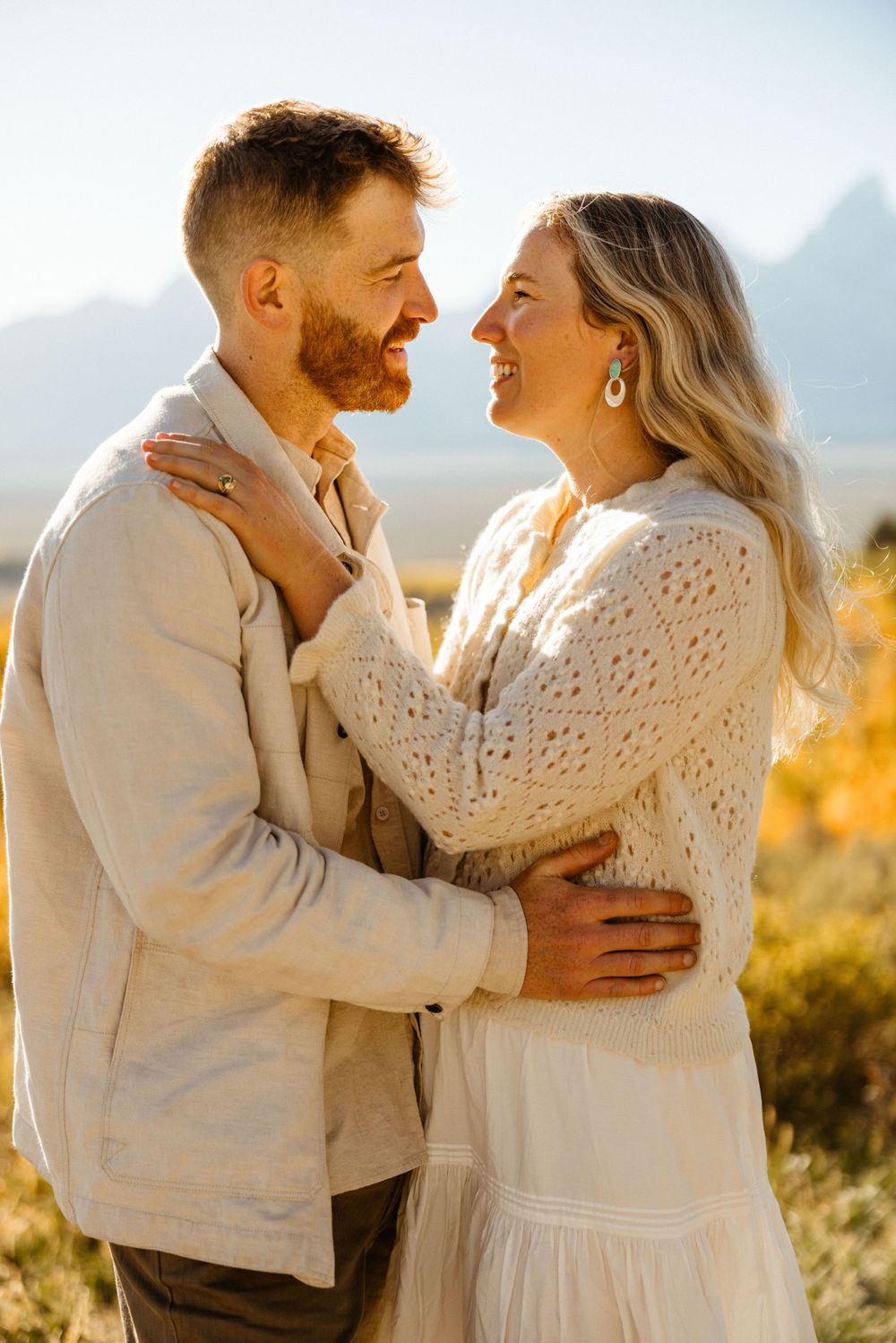 Intimate moment between a couple in white attire against a sun-drenched mountain landscape.