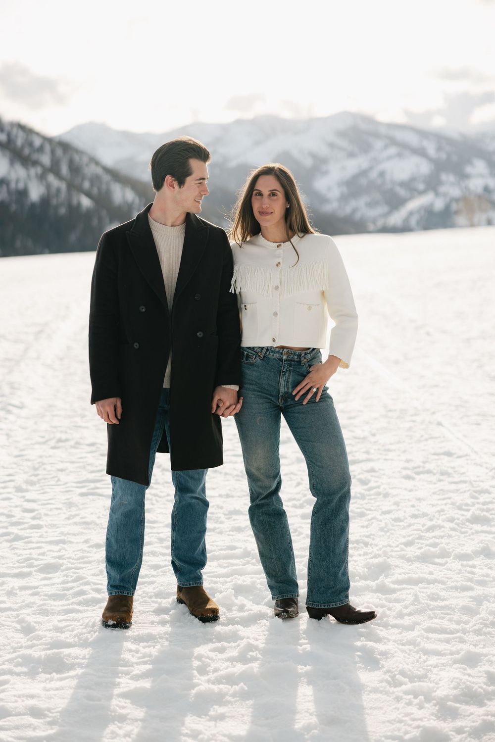 Couple poses together in snow with mountain landscape behind them.