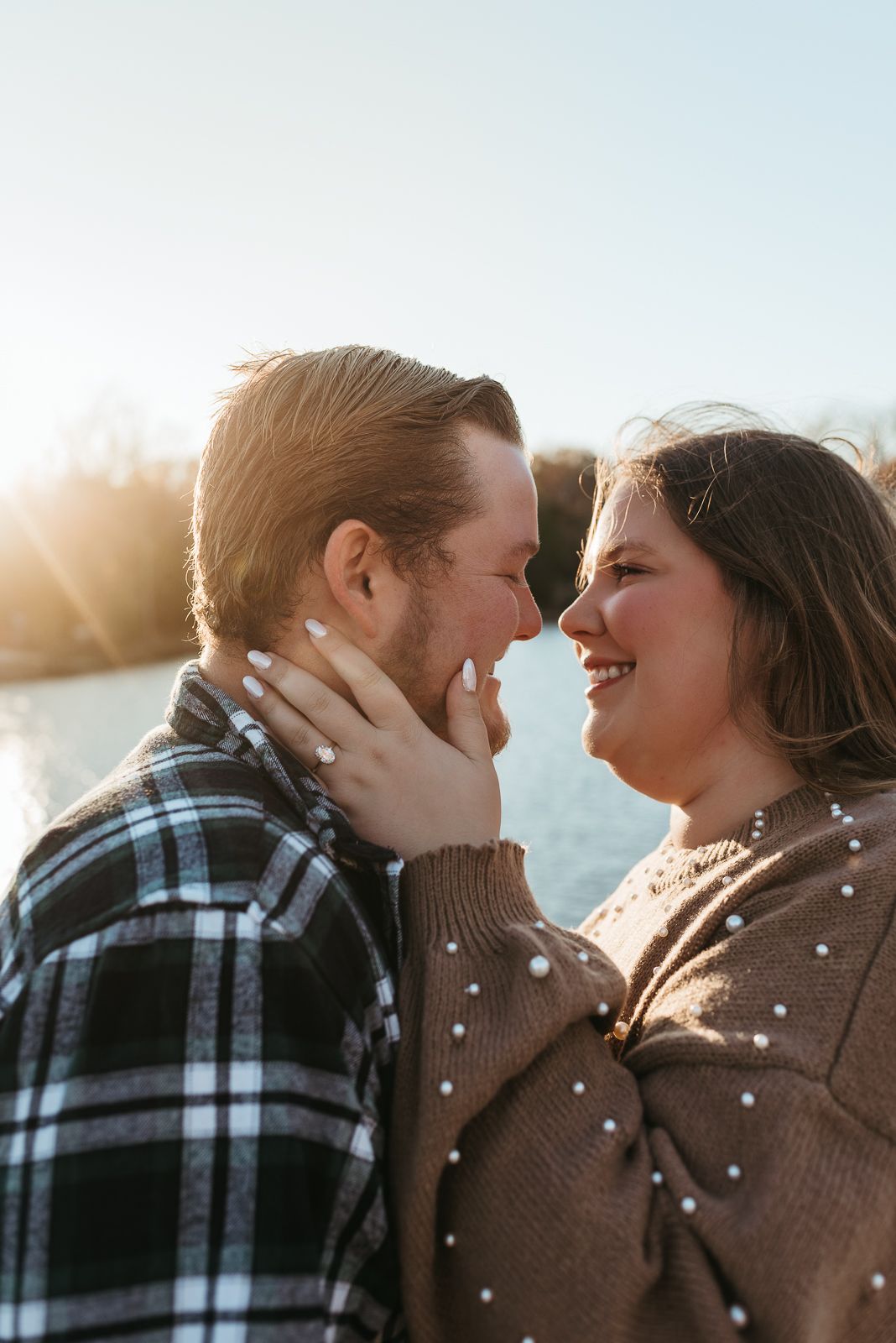 Romantic winter photoshoot with soft sunlight filtering through trees by a lake.