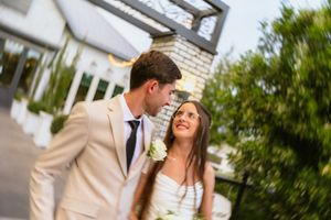 A bride and groom share a tender moment outdoors, with the groom in a beige suit and bride holding white flowers.