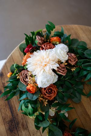 Elegant floral arrangement with white dahlias, brown roses, and eucalyptus on a wooden table.