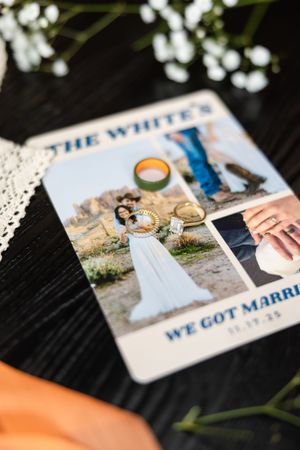 Wedding announcement card for The Whites featuring couple photos and rings on a dark wood surface with white flowers.