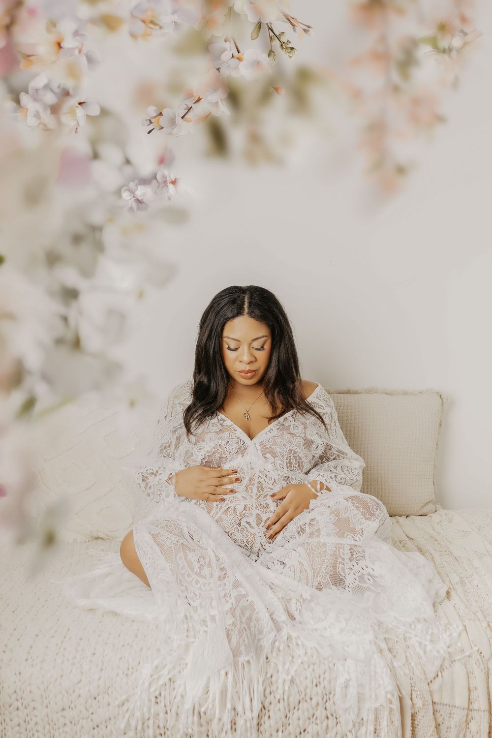 Woman in white lace dress relaxes on cream couch surrounded by soft floral elements.