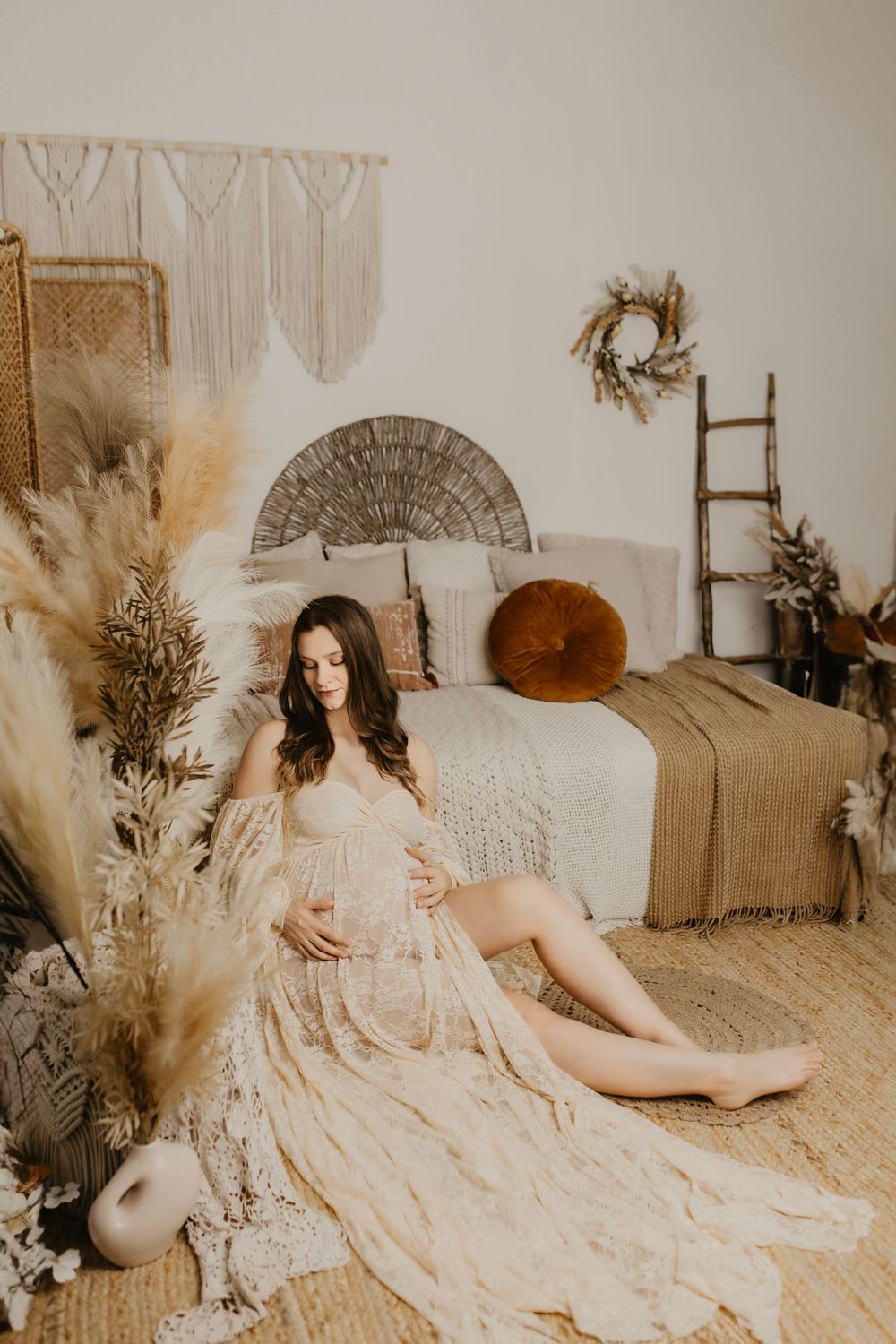 Ethereal maternity photoshoot featuring a flowing cream lace dress against a neutral boho-inspired backdrop.