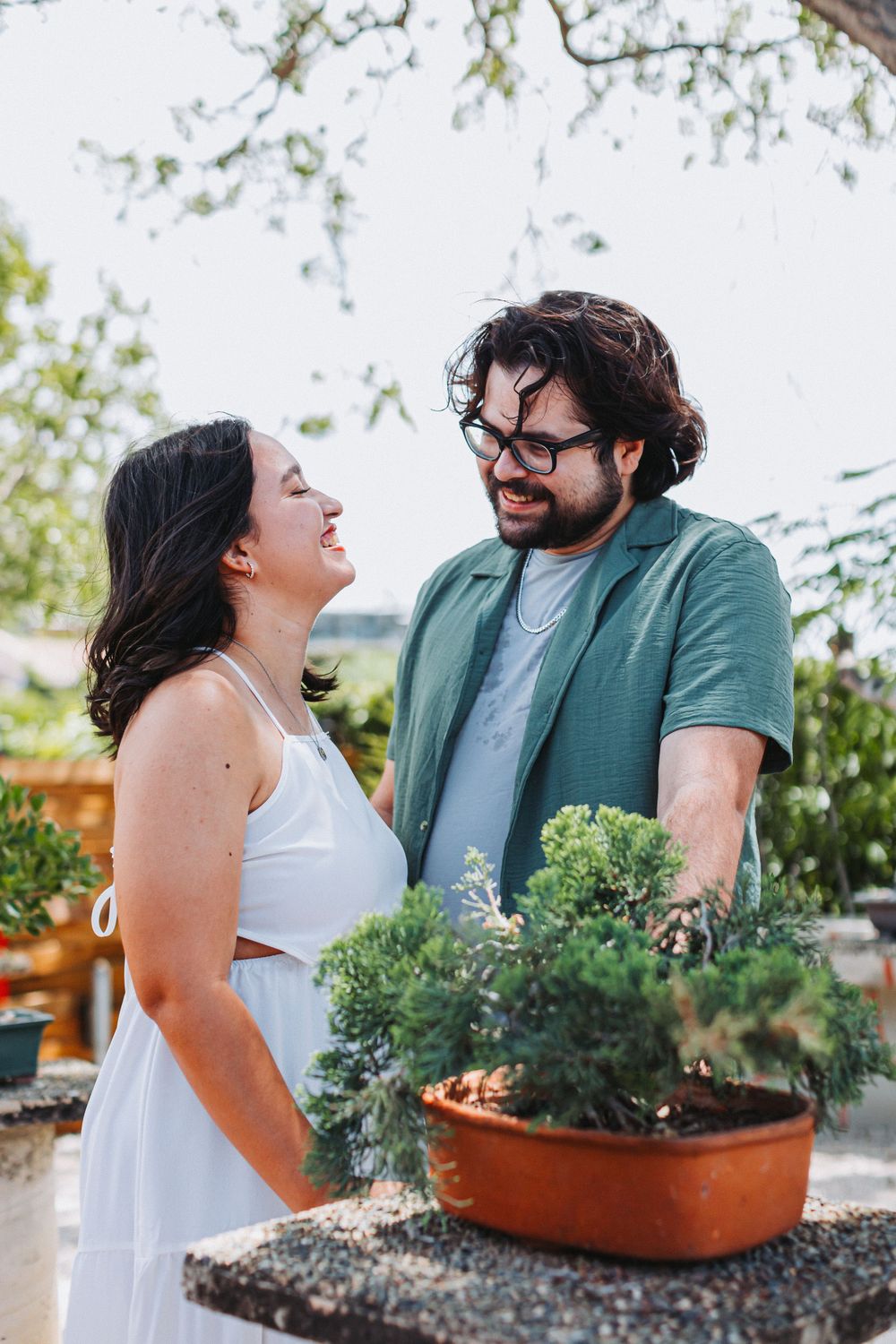 A couple shares a joyful moment while standing next to a potted plant in a garden setting.