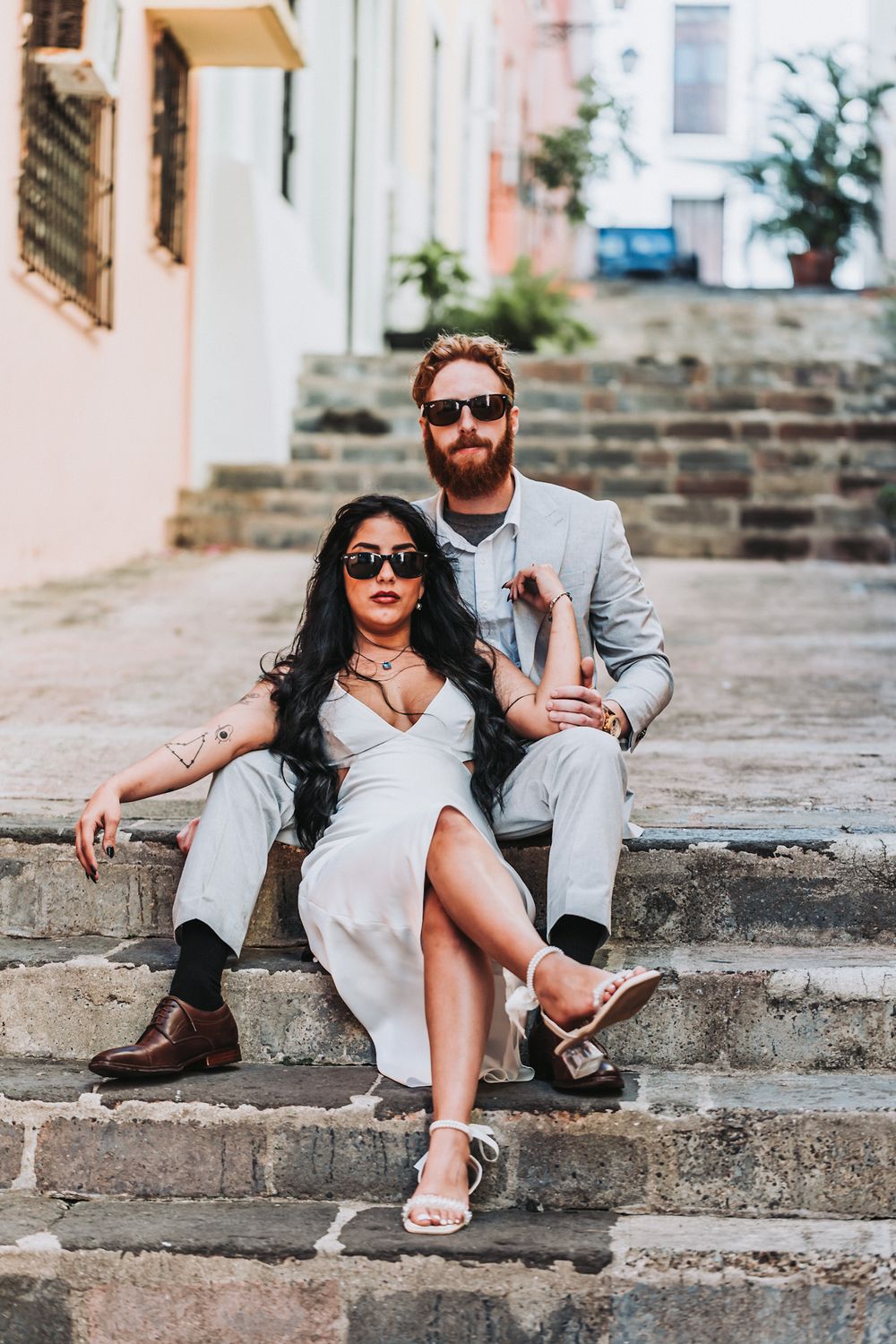 A stylish couple in light colored outfits poses on stone steps.