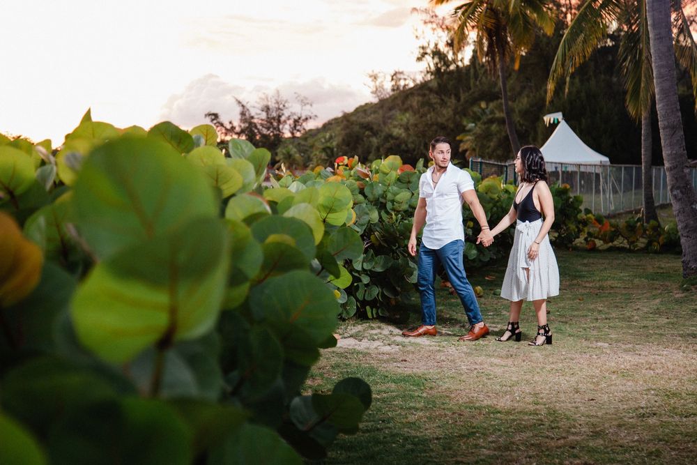 Couple holds hands walking through lush tropical garden at golden hour sunset.