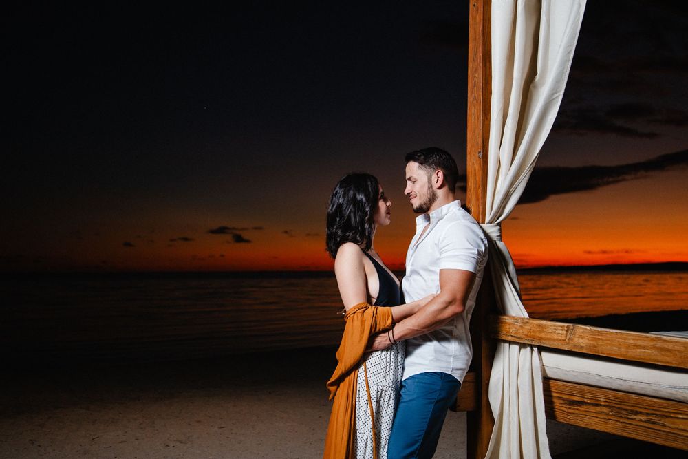 Romantic couple embracing at sunset on a beach, with vibrant orange sky and ocean in the background.