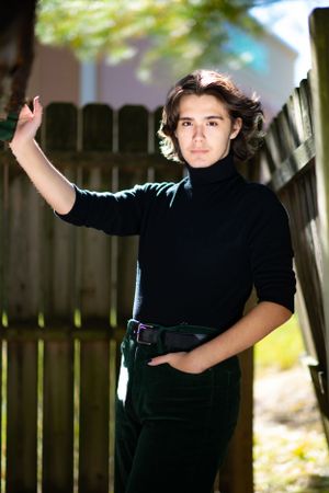 Dramatic portrait against wooden fence wearing black turtleneck in natural lighting.