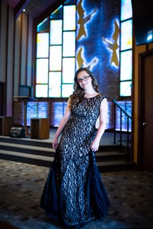 Formal portrait in navy lace gown inside church with stained glass windows.