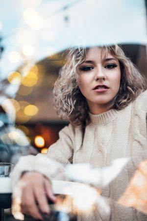 Stylish winter portrait with bokeh lights and cozy cream sweater in outdoor cafe setting.