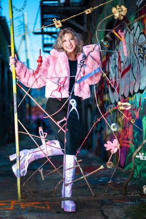 Creative portrait with pink jacket and platform boots against urban graffiti wall with string decorations.