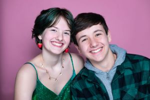 Twins pose together against a pink background wearing casual attire.