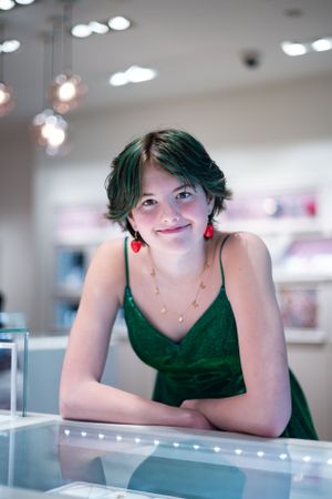 Portrait in emerald dress with cherry earrings against modern interior lighting.