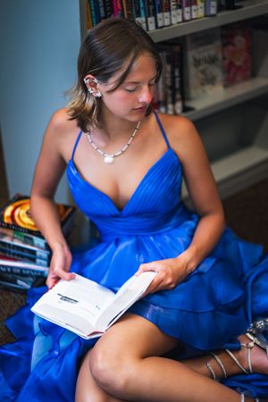 Young woman in blue prom dress reading a book in a library.