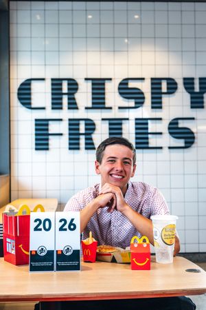 Young man smiling at McDonald's table with Happy Meal boxes near Crispy Fries sign.