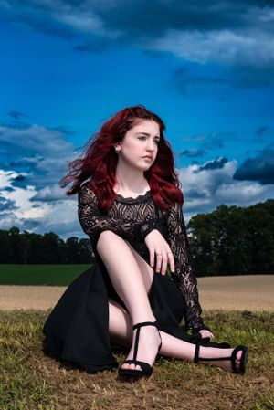A dramatic outdoor portrait against a blue sky featuring a black lace dress and striking red hair.