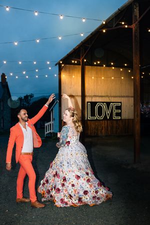 Dancing scene under string lights with neon LOVE sign at rustic outdoor wedding venue.