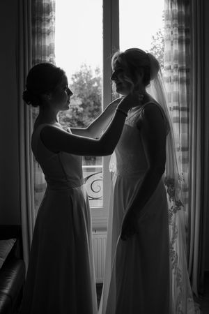 A series of silhouetted figures in white dresses stand near windows creating a dramatic black and white composition.