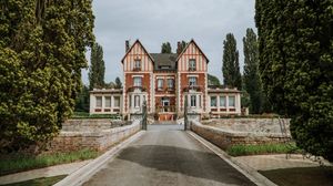 A panoramic view of a historic Victorian mansion with red brick architecture and manicured gardens.