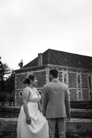 A black and white wedding photograph showing a couple standing in front of a historic brick building.