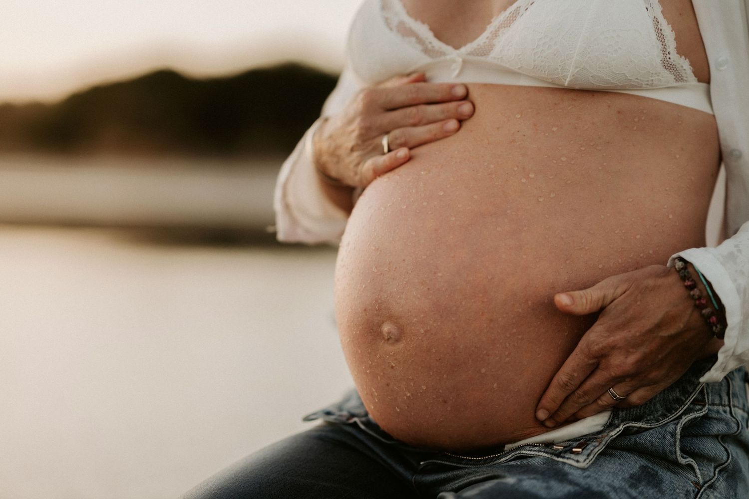 Close-up of pregnant belly in pink dress during golden hour at the beach.