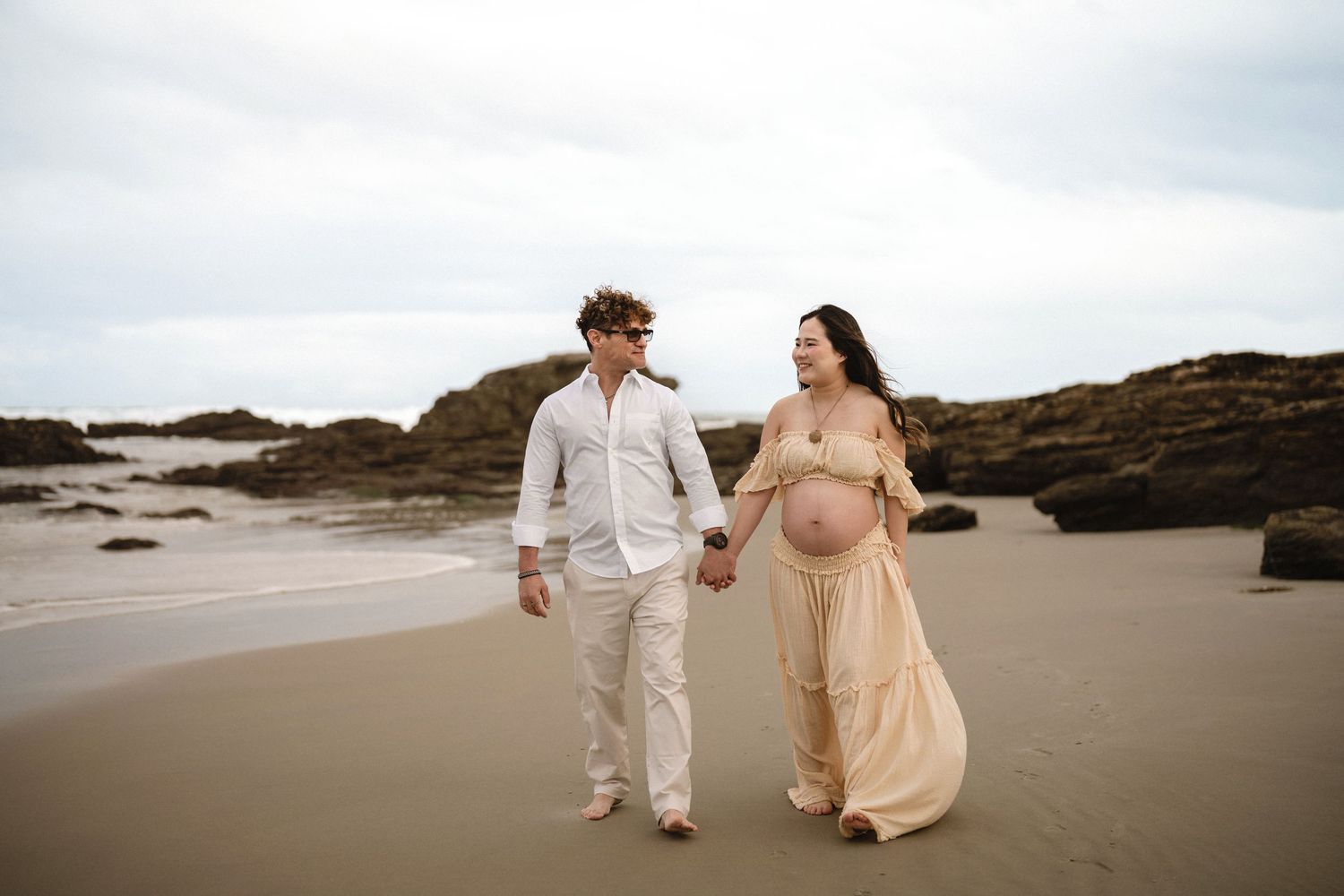 Close-up of pregnant belly in pink dress during golden hour at the beach.