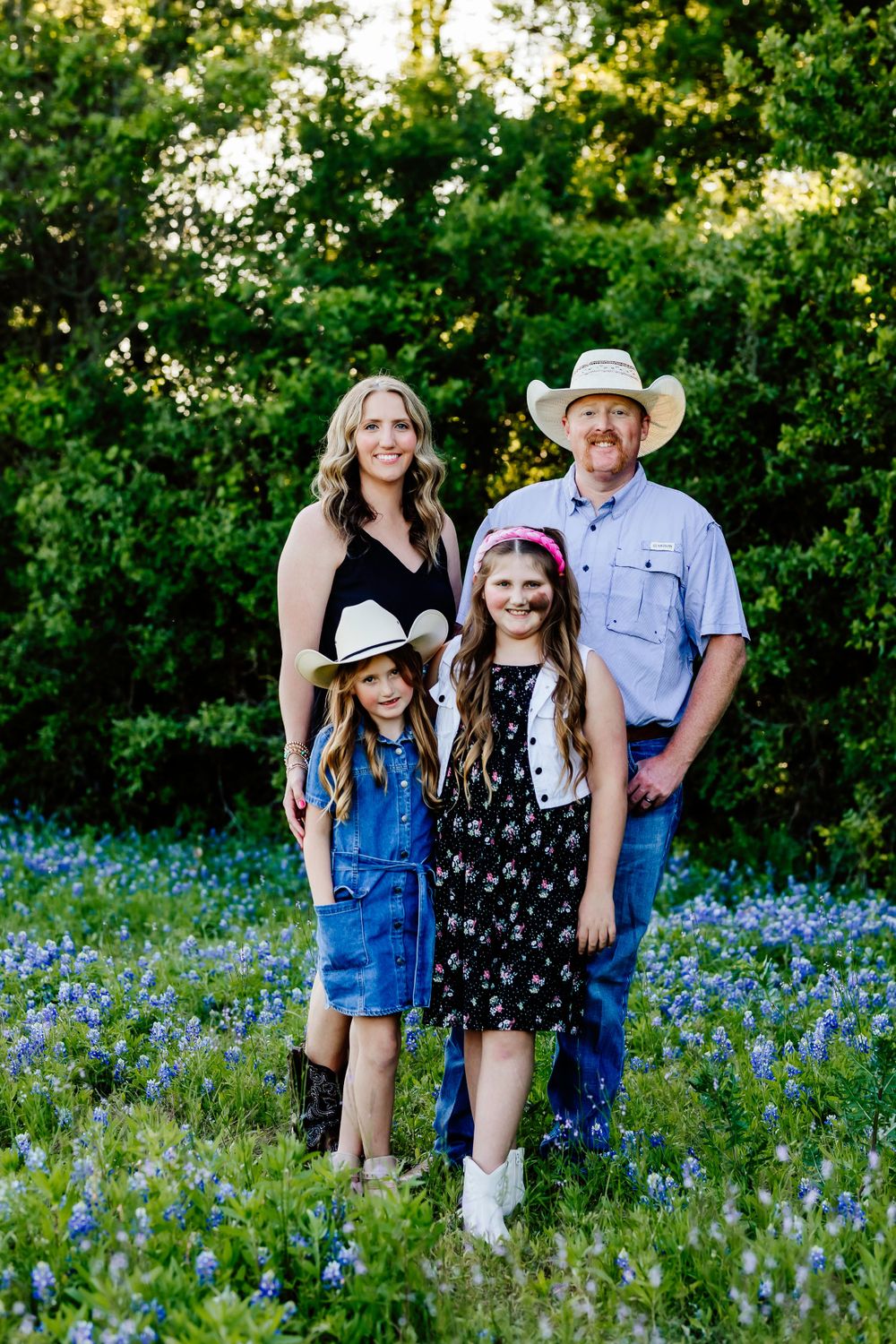 Family portrait in field of bluebonnets with green foliage background.