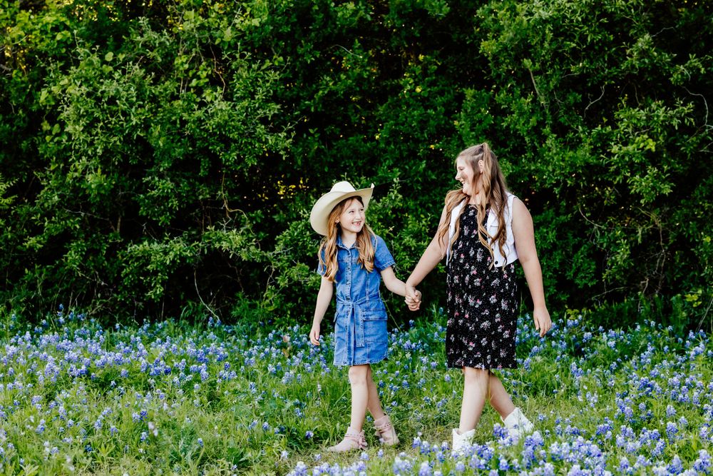 Two people walking hand in hand through a field of blue wildflowers.